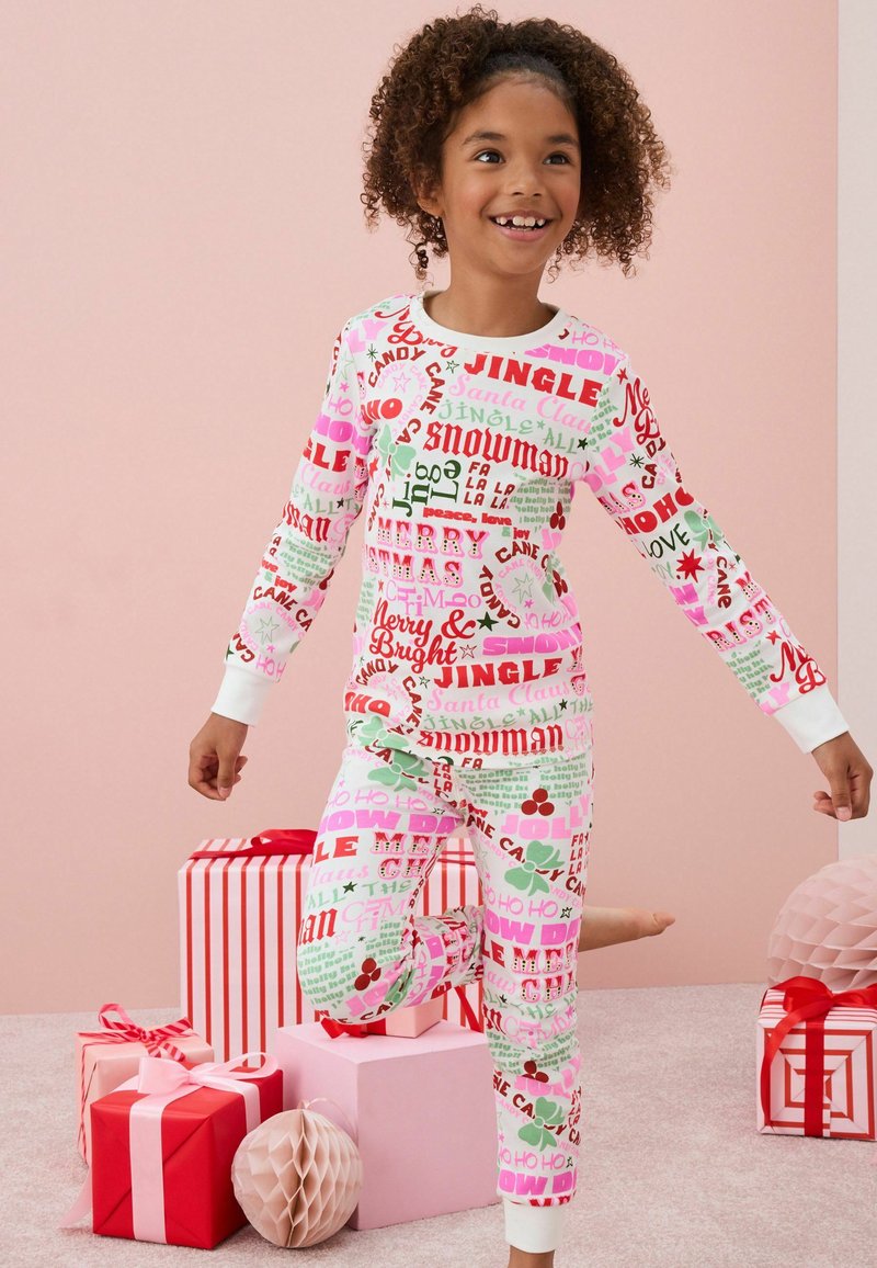 Röda, gröna och rosa mönstrade pyjamaser har festlig text ("Jingle", "Snögubbe") på en vit bakgrund, med vita manschetter och en figurnära design.