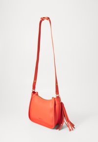 Red leather shoulder bag with a textured finish, curved shape, gold hardware, and a long strap featuring a tassel detail.