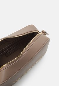 Hnědá kožená taštička se zlatým zipem, která má hladký povrch a označení značky uvnitř. Vnější strana má matný povrch.