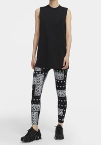 Svart ärmlös topp, parat med svarta leggings med vita geometriska och blommiga mönster; bärs med svarta sportskor.