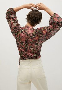 Blomstret bluse med lange ærmer i sort, med mønster af lyserøde og grønne roser, samt rynkedetaljer ved skuldrene og ryggen.