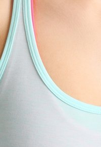 Gros plan d'une personne portant un débardeur bleu clair avec des bretelles roses visibles en dessous sur une épaule nue.