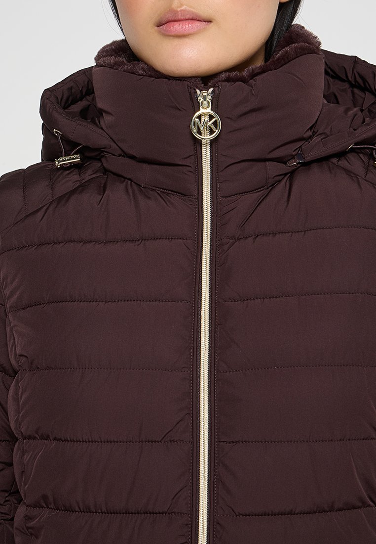 Veste matelassée bordeaux avec design en coutures, capuche doublée en fausse fourrure, fermeture éclair dorée avec accent logo et poches zippées sur les côtés.