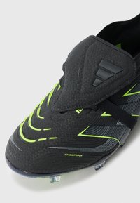 Black and neon green football boot with textured upper, elastic strap, and clear studs, labeled "HYBRIDTOUCH" on side.