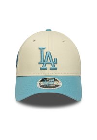 Gorra beige con visera azul claro y logo de LA. Cuenta con una correa ajustable, tejido texturizado y una etiqueta con logo redondo en el ala.