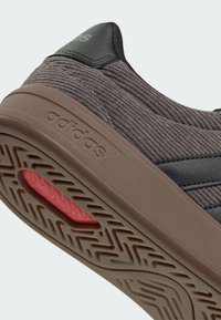Gros plan de la semelle marron d'une basket adidas avec une prise texturée, une insertion rouge et une tige en tissu côtelé avec des accents noirs.