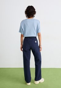 T-shirt en coton léger bleu clair à manches courtes, associé à un pantalon large bleu marine avec deux poches arrière et un petit logo.