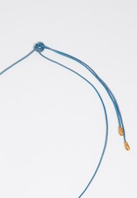 Collana in corda intrecciata blu con centro a nodo, con estremità in metallo dorato. Texture liscia con un contrasto di colori vivace.