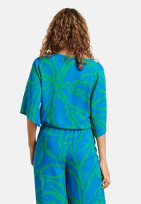 Blauwe blouse met een groen abstract patroon, losse pasvorm, brede mouwen en een gladde textuur, gecombineerd met bijpassende broek met een vergelijkbaar ontwerp.