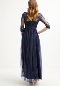 Nawigatorowy wieczorowy strój z koronkowym topem i rękawami do trzech czwartych, spływającą spódnicą z tiulu oraz marszczonym detalem w talii. Przezroczysty tył.