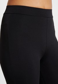 Svarta leggings gjorda av stretchmaterial, med hög midja och en jämn yta utan synliga sömmar eller mönster.