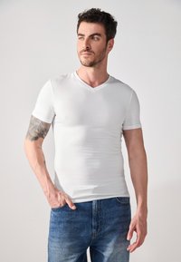 Bílý triko s výstřihem do V, ve fitted stylu, vyrobené z hladké tkaniny. Krátké rukávy, spárované s modrými džínami.