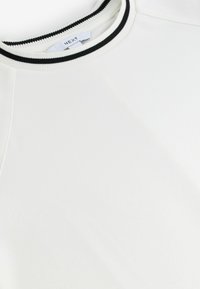 Biała bluza z okrągłym dekoltem, ozdobiona czarno-białym prążkowanym wykończeniem, o gładkiej fakturze i dekoracyjnym przeszyciu.