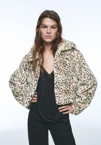 Jakke i leopardmønsteret imiteret pels med krave, kort design og lynlåslukning. Båret over en sort top og kombineret med mørke bukser.