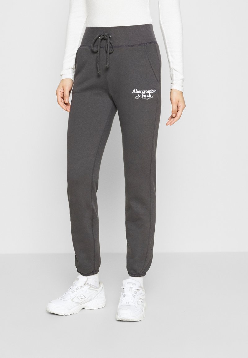 Dunkelgraue Jogginghose mit Kordelzugbund, Seitentaschen und einem gestickten weißen Logo auf dem oberen linken Oberschenkel. Angenehme, glatte Textur.