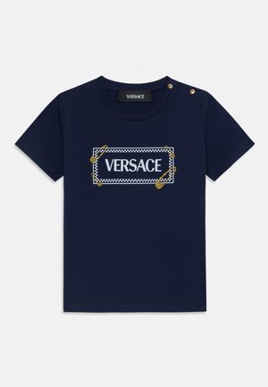 Tumed puuvillane T-särk, millel on ümmargune kaelus, esipaneelil valge "VERSACE" logo, mida ümbritseb ruuduline muster, kaunistatud kuldsete ohutuspinkidega.