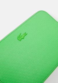 Grünes, strukturiertes Portemonnaie mit erhabenem, geprägtem Logo. Rechteckige Form mit abgerundeten Kanten und sichtbarem Stichdetail.