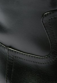 Stivale in pelle nera con una texture liscia, caratterizzato da cuciture dettagliate e una leggera lucentezza. Accentuato da un design impresso sul lato.
