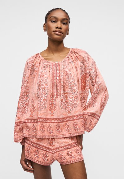 Jeune femme portant un chemisier ample à manches longues couleur pêche et un short assorti à motifs complexes floraux et cachemire.