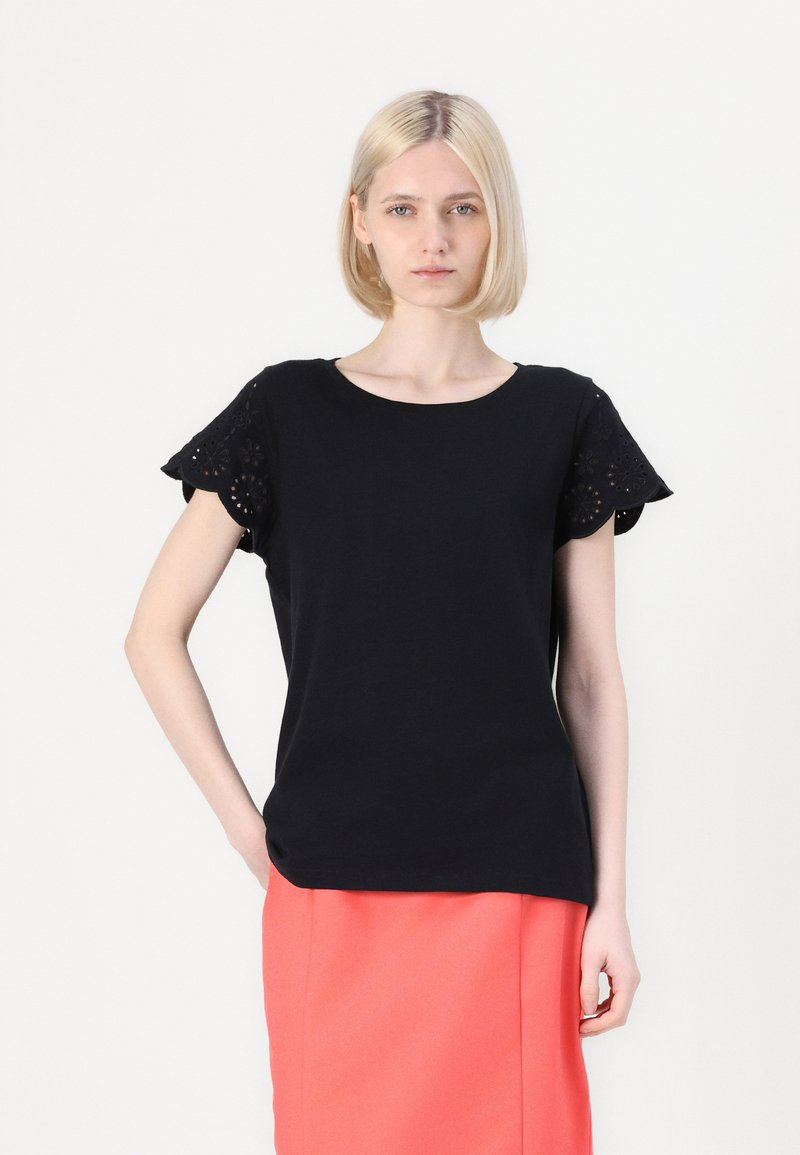 T-shirt en coton noir avec des manches en œillet festonné, associé à une jupe crayon corail. Encolure ronde simple, coupe décontractée.