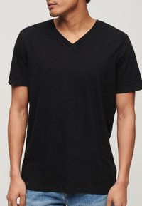 Czarny bawełniany T-shirt z dekoltem w serek i krótkimi rękawami; miękka faktura i luźny krój. Noszony z jasnoniebieskimi dżinsami.