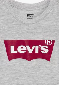 T-shirt gris à col rond avec un grand logo rouge Levi's imprimé sur la poitrine et une petite étiquette Levi's à l'intérieur du col.