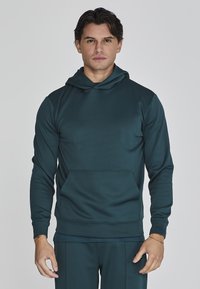 Sudadera azul oscuro hecha de una tela suave y lisa. Cuenta con un bolsillo tipo canguro en la parte frontal y una capucha ajustable con cordón. Diseño entallado con puños de canalé.