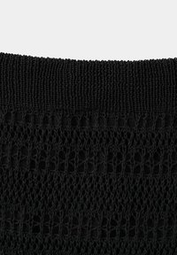Tissu tricoté noir avec une taille côtelée et des motifs en dentelle ouverts et complexes sur tout le matériau.