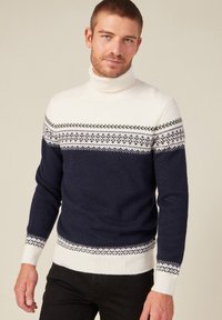 Pull col roulé bleu marine avec ourlet et poignets côtelés, partie supérieure couleur crème et accents à motifs complexes en gris et blanc.