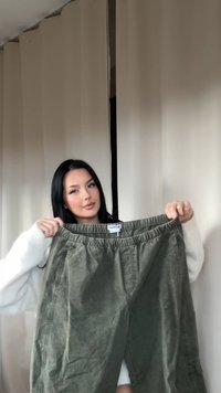 Pantalones verdes oliva con cintura elástica, fabricados en tejido texturizado, que presentan un corte holgado y detalles en las costuras laterales, sostenidos por una persona.