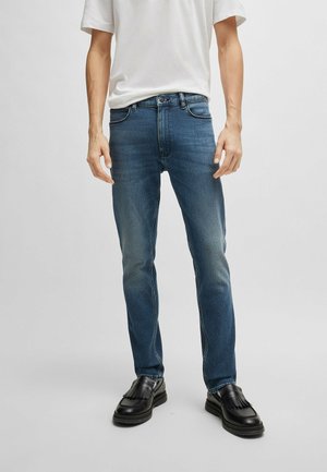 Jeans in denim blu con una vestibilità slim, cinque tasche e leggere scoloriture. Abbinati a scarpe nere con dettaglio frangia.