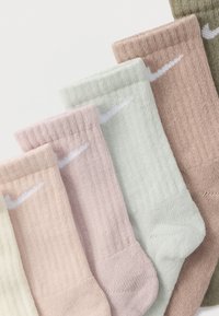 Fem par ribbede Nike-strømper i pastelfarverne creme, lyserød, mintgrøn, mauve og olivengrøn arrangeret overlappende.