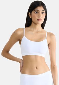 Witte naadloze bralette met dunne bandjes, een brede band en een gladde textuur. Heeft een minimalistisch ontwerp, geschikt voor lagen en comfort.