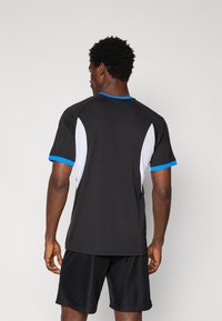 Tricou sport negru cu accente albastre și panouri laterale din plasă albă. Are un guler rotund și mâneci scurte, fiind realizat dintr-un material respirabil.