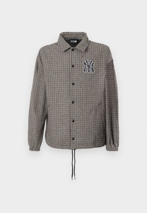 Sako s kostkovaným vzorem houndstooth v šedé a černé barvě, s předním zapínáním na knoflíky, elastickými manžetami a vyšitým logem na hrudi.