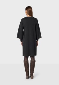 Abito nero al ginocchio con maniche larghe e design dritto. Indossato con stivali in camoscio marroni fino al ginocchio e collant trasparenti.