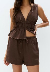 Débardeur en lin brun avec un décolleté en V profond et un ourlet effiloché, associé à un short assorti doté d'une taille élastique et d'un cordon de serrage.