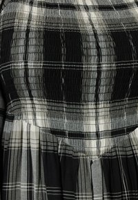 Mustikka, valkoinen ja harmaa ruudullinen kuvio, jossa on nyöritetty yläosa, teksturoitu pinta ja soljuva hame, jossa on laskoksia.