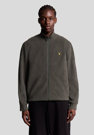 Fleece zip-jakke i mørk olivengrøn med høj krave, der har et lille gult logo på brystet og ribbede manchetter.