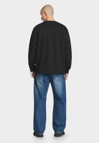 Czarna koszula z długim rękawem o okrągłym dekolcie, w zestawie z luźnymi niebieskimi dżinsami z wyblakłymi łatami i standardowym pięciopocketowym fasonem.