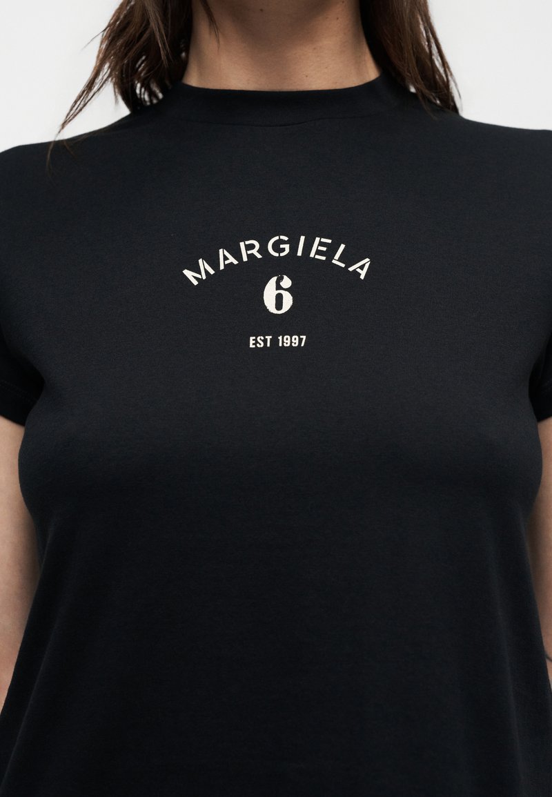 Black short-sleeve t-shirt with white "MARGIELA 6 EST 1997" text centered on the chest, worn by a person with long hair.