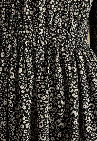 Schwarzer Stoff mit kleinen weißen unregelmäßigen Blumenmustern und gerafftem elastischem Detail, das Rüschen und Textur erzeugt.