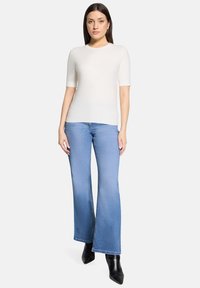 Haut court ajusté crème à manches courtes associé à un jean bleu clair évasé taille haute. Des bottines à talons noires complètent le look.