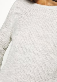 Ljust grått stickat tröja med ett texturerat mönster, rund halsringning och långa ärmar med ribbade muddarna. Mjuk, luftigt tyg.