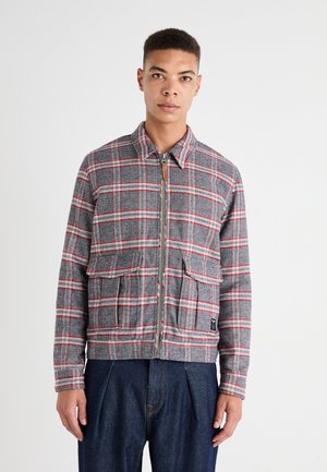 Chaqueta de cuadros gris y rojo con cremallera y cuello, dos bolsillos frontales y un acabado texturizado, complementada por un corte recto en la parte inferior.