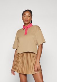 Μπεζ κοντομάνικο πόλο μπλουζάκι με ροζ γιακά και κουμπιά, σε συνδυασμό με φούστα σε ταν απόχρωση με πτυχώσεις, που αναδεικνύει σχέδιο υφής.