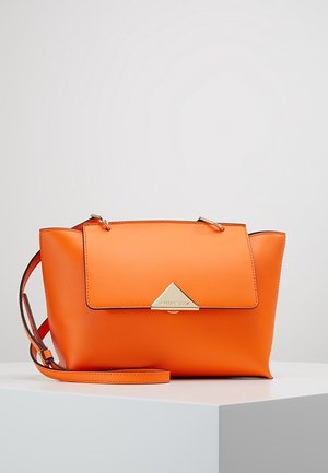 Lyseorange læderhåndtaske med gyldent trekantet spænde og justerbar skulderrem, vist på en hvid overflade mod en ensfarvet baggrund.