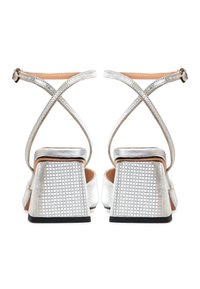 Silver high-heeled sandals with cross straps and textured surfaces. Square heels have a grid pattern and a contrasting black base.