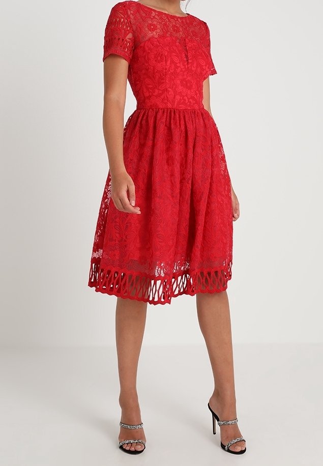 Rotes Spitzenkleid mit kurzen Ärmeln, floralem Muster, tailliertem Oberteil, ausgestelltem Rock und Ausschnitt am Saum. Getragen mit silbernen Riemchenabsätzen.