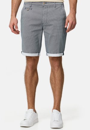 Herren-Chino-Shorts mit einem hellblauen Hahnentrittmuster, ausgestattet mit umgeschlagenen Säumen, Seitentaschen und einem Knopfverschluss. Kombiniert mit weißen Sneakern.